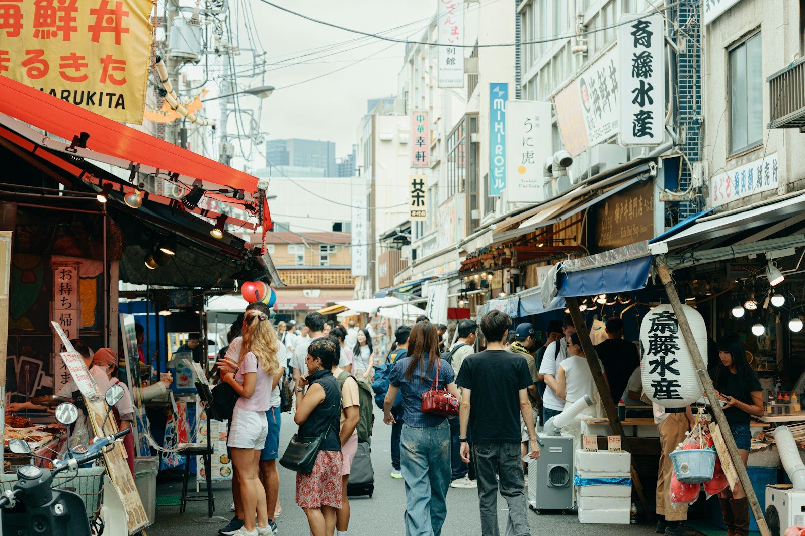 People walking through a narrow street market in Tokyo lined with food stalls