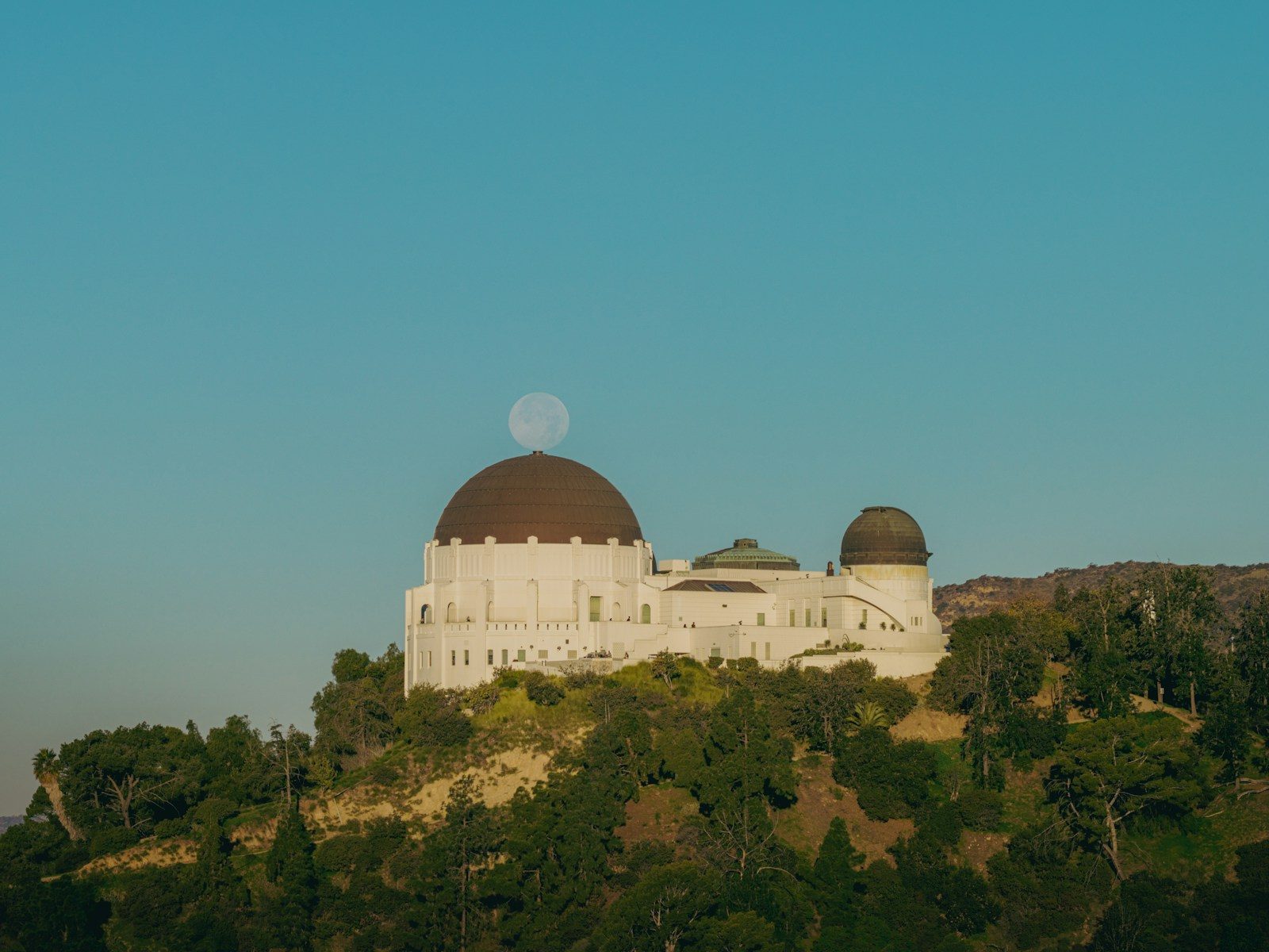Griffith observatory building with moon behind dome